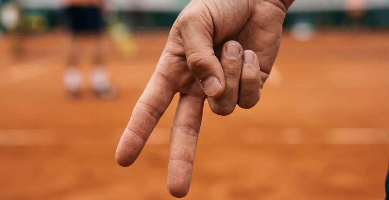 Gros plan sur les mains d'un joueur de tennis faisant un signe tactique derrière son dos, texture de la peau et détails des doigts
