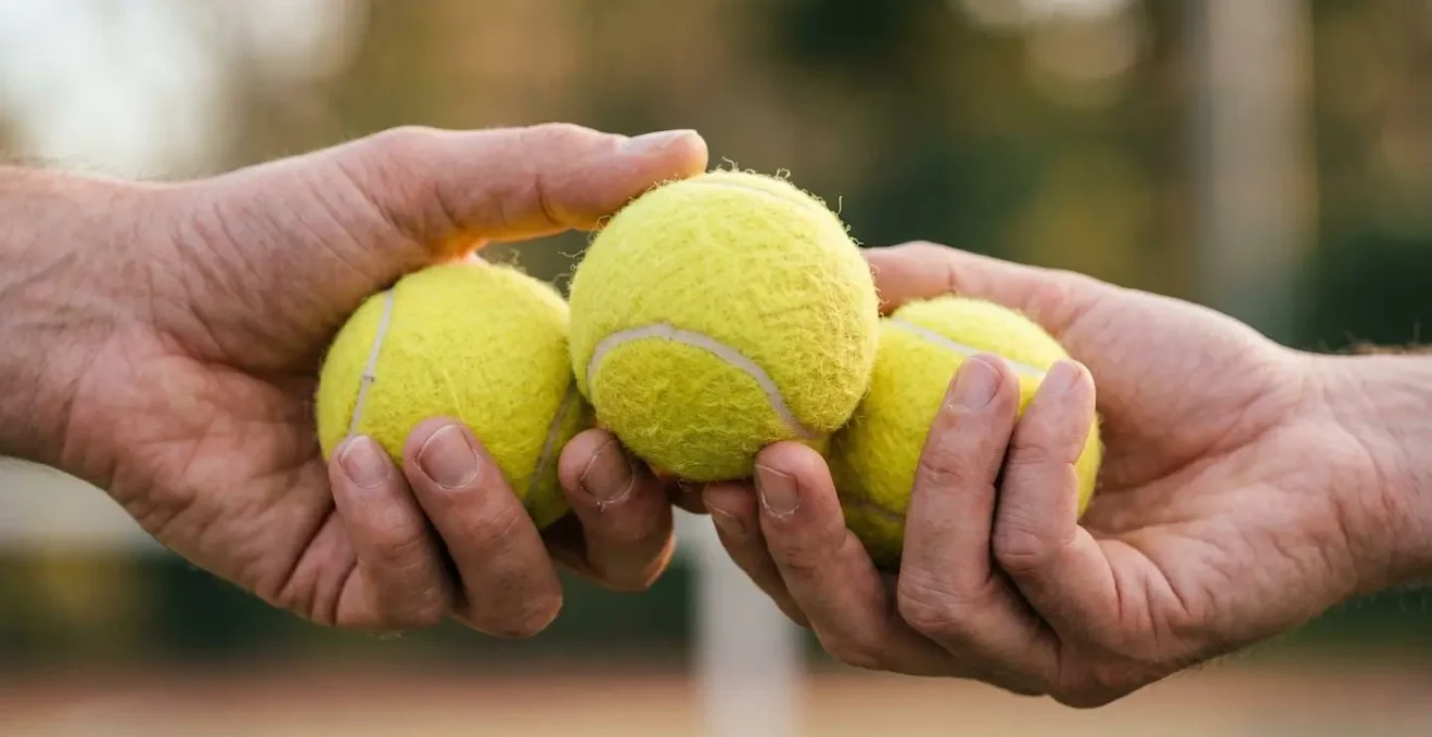 Gros plan sur deux mains échangeant des balles de tennis jaunes dans une lumière naturelle douce