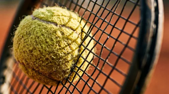 Gros plan sur une raquette de tennis cordée avec une balle en impact, illustrant la maîtrise technique et la régularité dans la frappe