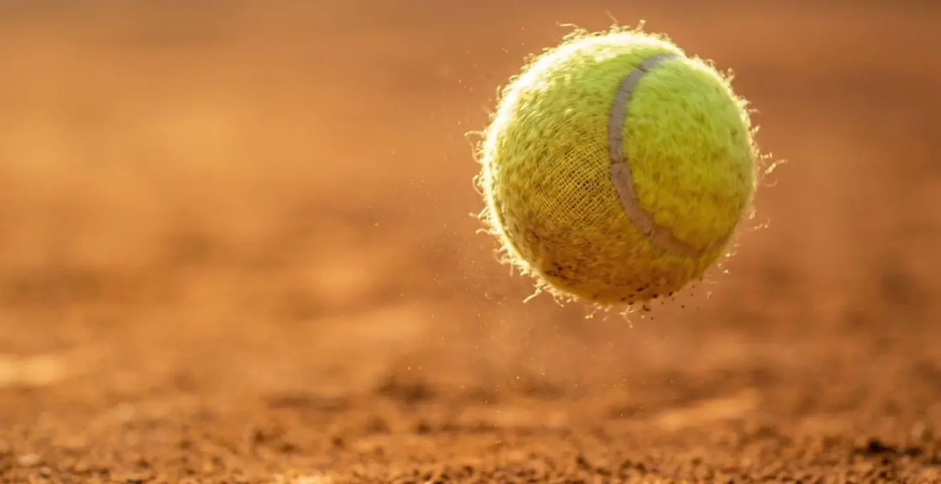 Gros plan sur une balle de tennis en pleine rotation liftée capturée en plein vol au-dessus d'un court de terre battue ocre