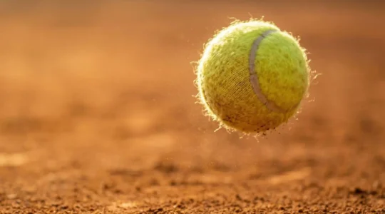 Gros plan sur une balle de tennis en pleine rotation liftée capturée en plein vol au-dessus d'un court de terre battue ocre